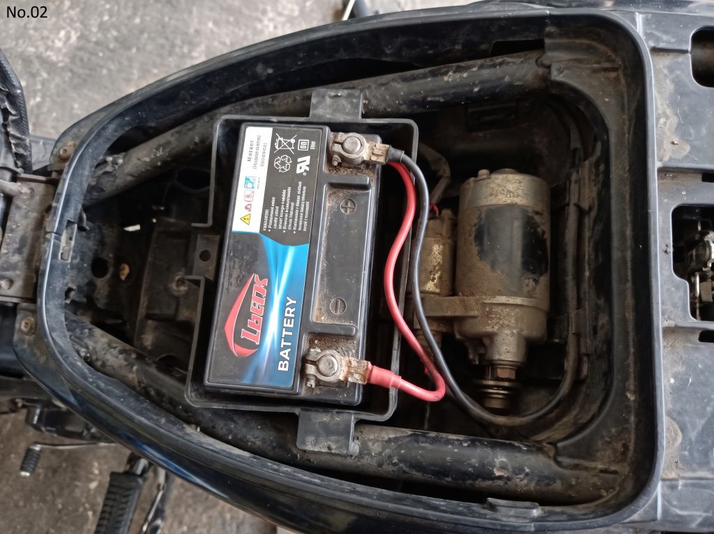Aki dengan terminal dan kabel pada kompartemen motor yang terbuka.
