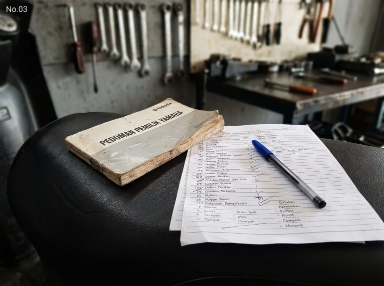 Buku pedoman, lembar catatan, dan pena di area kerja.